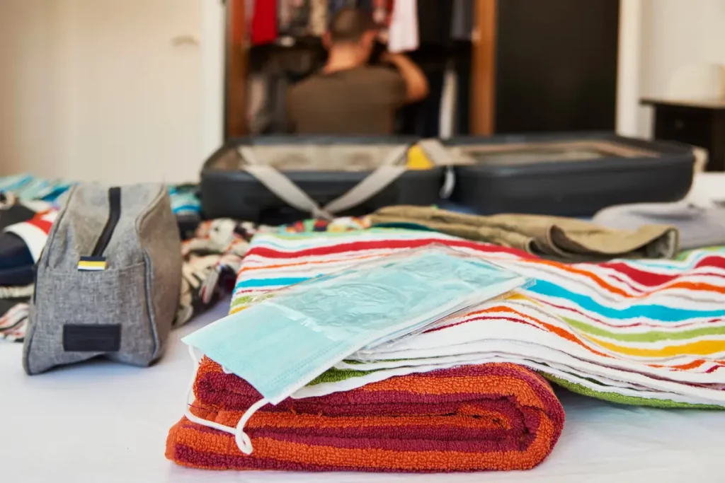 mala e roupas em cima da cama. Homem ao fundo mexendo no guarda roupa